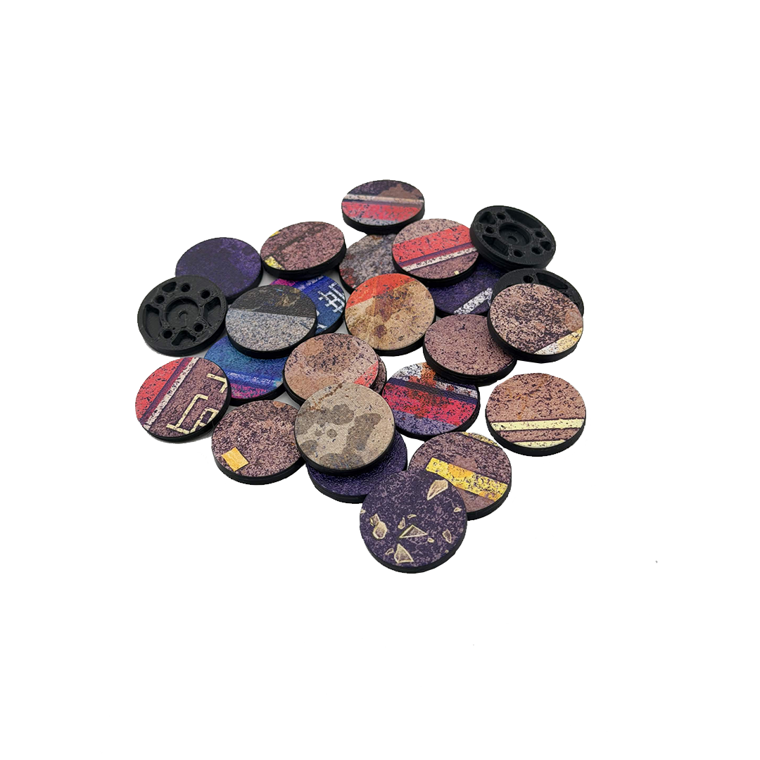 A pile of round, printed 27mm bases with various patterns and colors, including purple, red, blue, yellow, and black, on a plain white background.
